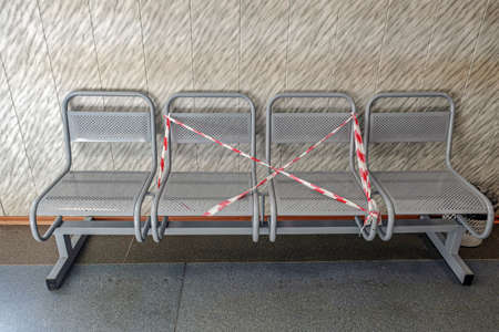 a four-seater metal bench in a public place with two seats covered with a signal tape for...