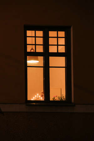 a window lit in the night with a decorative lamp burning with seven candles on the windowsillの写真素材