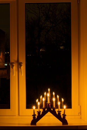 electric decorative light on the windowsill, burning with seven candles reflecting in a dark windowの写真素材