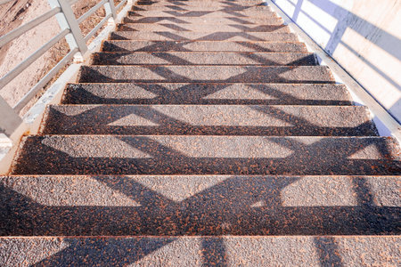 Shadows from handrails on an iron staircase in asphalt steps leading down