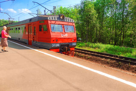 June 18, 2020, Russia, St. Petersburg, a suburban electric train approaches the platform, a woman in a mask and gloves is walking towards itのeditorial素材