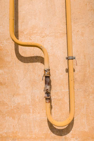 yellow curved pipe with rusty faucet on old wall with scratchesの写真素材