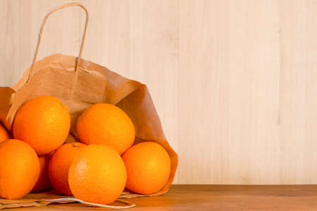 ripe oranges in a paper bag on a wooden tableの写真素材
