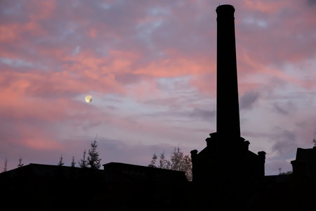 silhouette of an industrial chimney and a full moon against the background of the dawn skyの写真素材