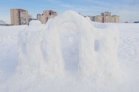 Fortress made of snow with windows and an entrance against the backdrop of city houses in the...