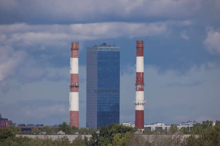 Cityscape: Two industrial chimneys flanking a high-rise building overlooking a city under a cloudy...