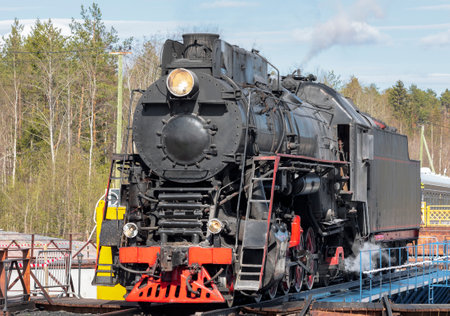 Black steam locomotive with a burning spotlight on a turning circle against the backdrop of a green...