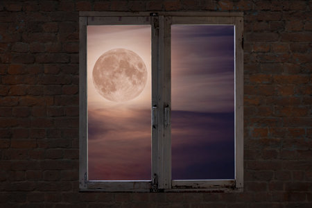 View of the full moon in the clouds through an old window in a brick wall