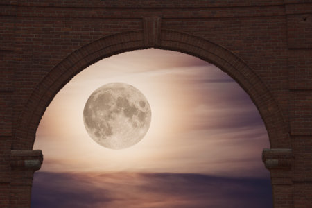 view of the full moon illuminating the clouds in the night sky through a brick archの写真素材