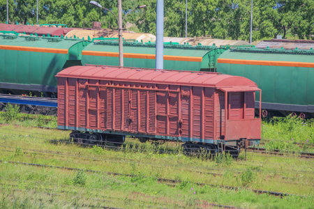 a lonely covered freight car at a railway station in front of trainsの写真素材