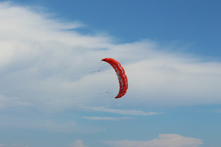 red parachute flying in blue sky with white cloudsの写真素材