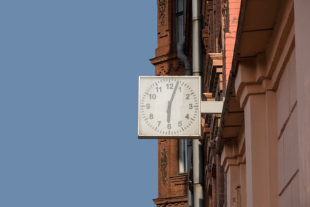 A street clock on the wall showing six o'clock, three minutes