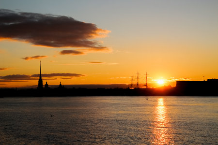 Silhouettes of city buildings against the backdrop of the setting sun, reflected in the waters of...