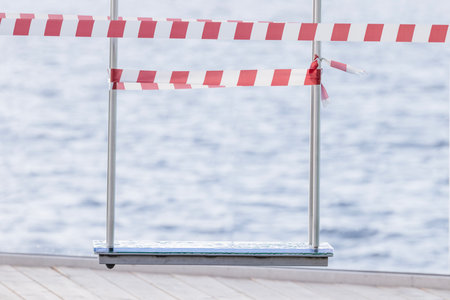 A wet swing after the rain, fenced off with white and red warning tape.の写真素材