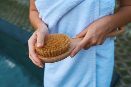 A brush for dry massage in the hands of a girl on the background of a towel. Brush for cleansing the body of cellulite and orange peel.の写真素材