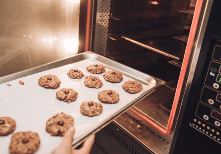 Woman taking baking tray with delicious oatmeal cookies out of ovenの写真素材