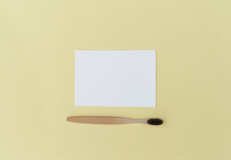 An empty paper sheet card with a model copy space and a wooden toothbrush, on a yellow background. Minimum business brand template zero waste. Top Viewの写真素材