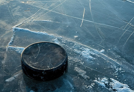 Detailed close-up of a used hockey puck on a textured ice surface, a monochrome image that captures the essence of winter sportsの素材