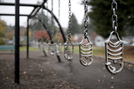Several swings hang empty in a playground, surrounded by a soft, cloudy sky. The park features vibrant autumn foliage, creating a serene atmosphere.の素材