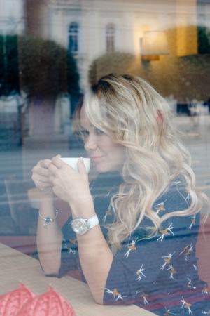 Beautiful girl inside a cafe with cup of coffe sitting at the windowの写真素材