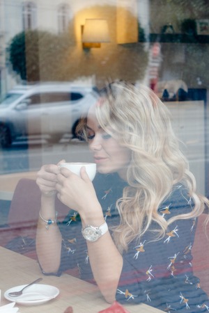 Beautiful girl inside a cafe with cup of coffe sitting at the windowの写真素材