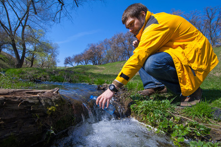 man taking bottle of water from a mountain stream. Enjoying the outdoors in the summer trekking...