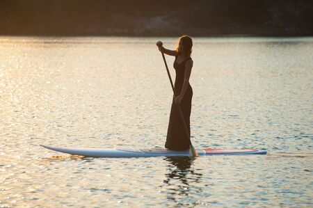 The girl in a black dress with a paddle board floats on waterの写真素材