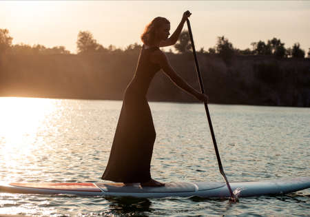 stand up paddle board performed by beautiful girl on the sunset backgroundの写真素材