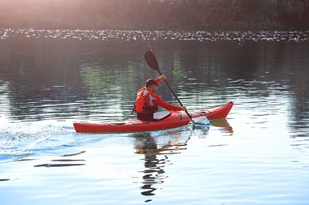 man paddles a red kayak on the river near the shore, kayakingの写真素材