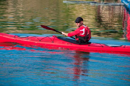 man paddles a red kayak on the river near the shore, kayakingの写真素材