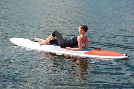 stand up paddle board yoga performed by beautiful girl on the bright city background, yoga training...