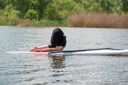 stand up paddle board yoga performed by beautiful girl on the bright city background, yoga training on the beachの写真素材