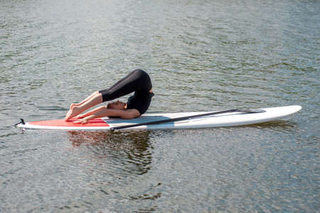 stand up paddle board yoga performed by beautiful girl on the bright city background, yoga training on the beachの写真素材