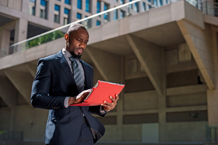 black man in a business suit standing street and uses phones and tablet computerの写真素材