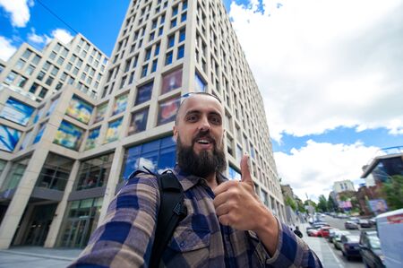 young bearded man showing a thumbs up makes selfie on the city background , self portrait pictureの写真素材