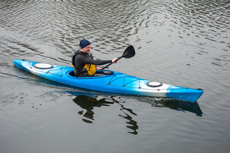 man paddles a blue kayak on the river near the shore, kayaking
