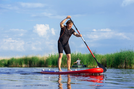 SUP stand up athletic man with a paddle on the red board
