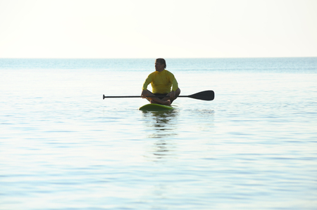 SUP silhouette of athletic man standing with a paddle on the surfboard at sunset stand up paddle boardingの写真素材