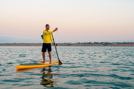 man in sportswear makes a photo setting sun on the action camera stand up paddle boardingの写真素材