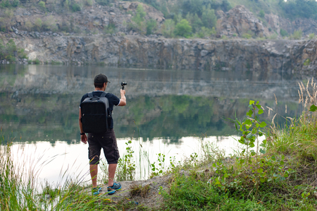Back view of man taking pictures of beautiful lake on action camera while traveling in wild natureの写真素材