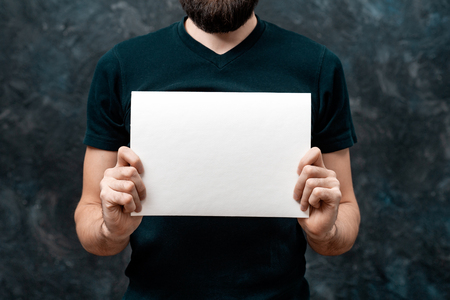 Cropped image of guy in dark T-shirt showing blank paper sheet with copy space for your announcementの写真素材