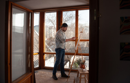 Side view of male creator painting on canvas while standing in workshop with panoramic windowsの写真素材