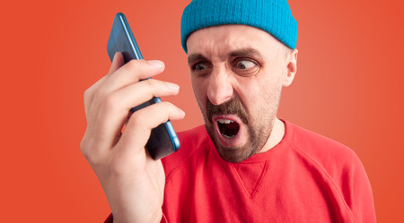 Close up portrait of rude man screaming and swearing at someone with grimace of anger while talking...