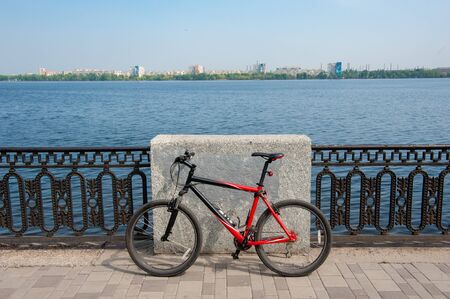 Close up photo of red bike placed on pavement and leaned on street barrier on embankmentの写真素材