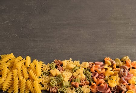 
Raw pasta of different colors and types laid out on a dark wooden table below photoの写真素材