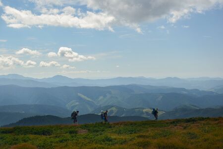 A family of three people travel with backpacks on top of a mountain and in the background sky and mountainsの写真素材