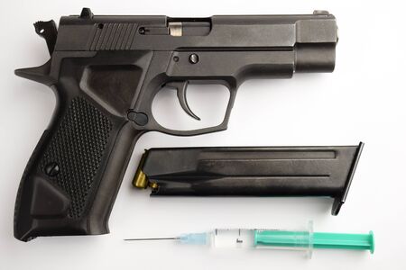 The black gun lies with a clip and a plastic syringe with a needle on a white background