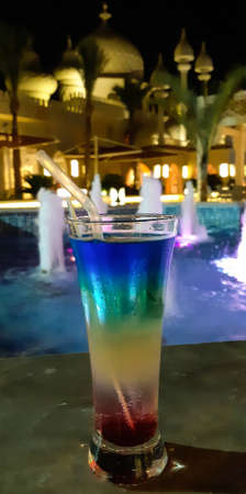 A glass with a multi-colored cocktail is on the table in the hotel. On a blurred background of a...