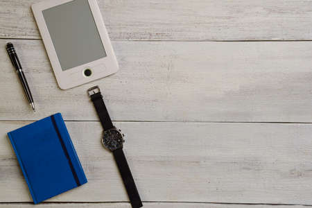 An e-book, a wrist watch, a diary and a pen lie on a wooden table. There is an empty space on the...
