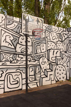 A basketball basket and backboard stand on a sports field against a painted wall with graffiti and...